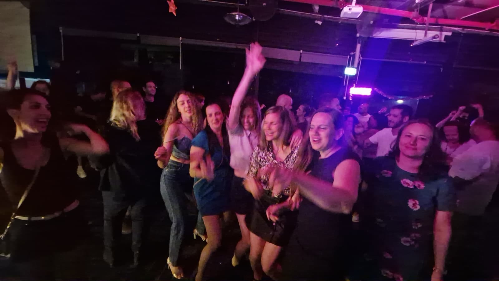 רחבת ריקודים מלאה, נשים וגברים רוקדים ומצטלמים במסיבה
