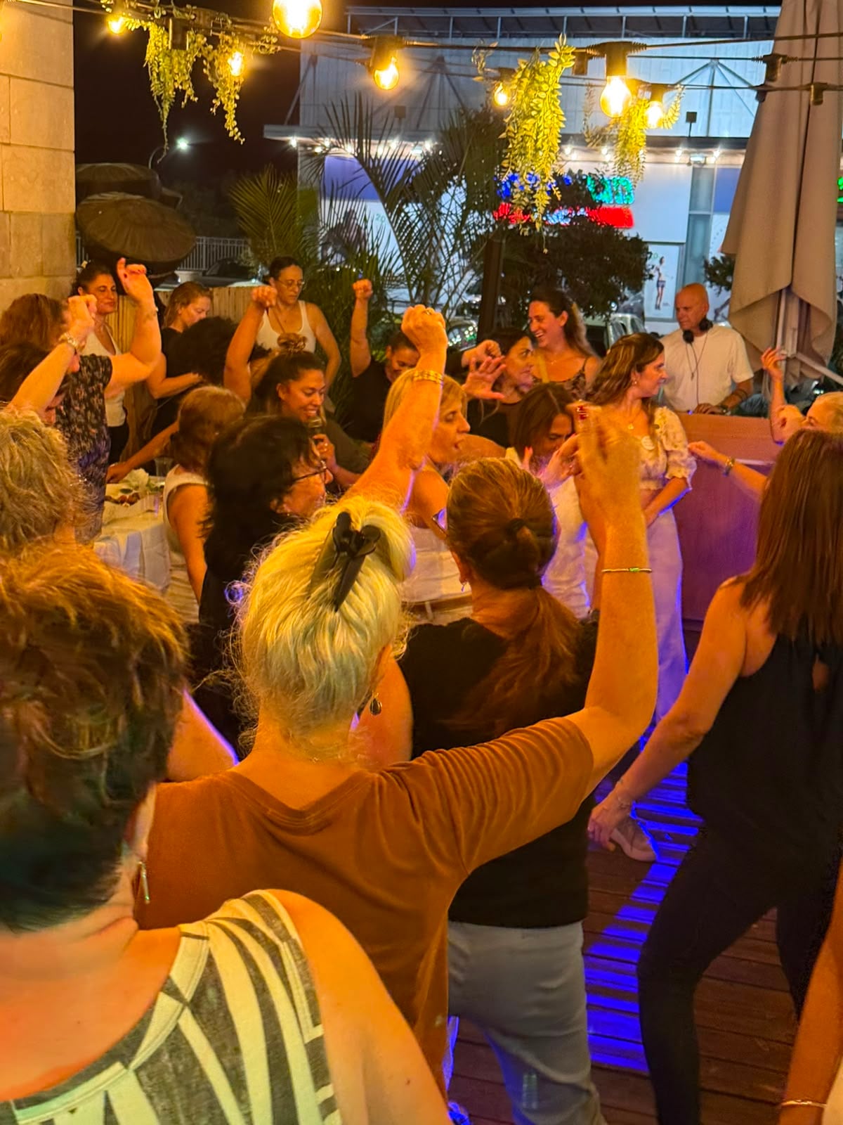רחבה מלאה בנשים רוקדות עם ידיים מורמות, באורות צבעוניים