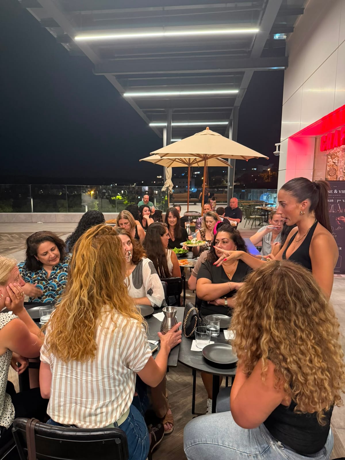 הפעלה בערב שני נשי, אישה עומדת ומדברת אל השולחן והנשים מקשיבות