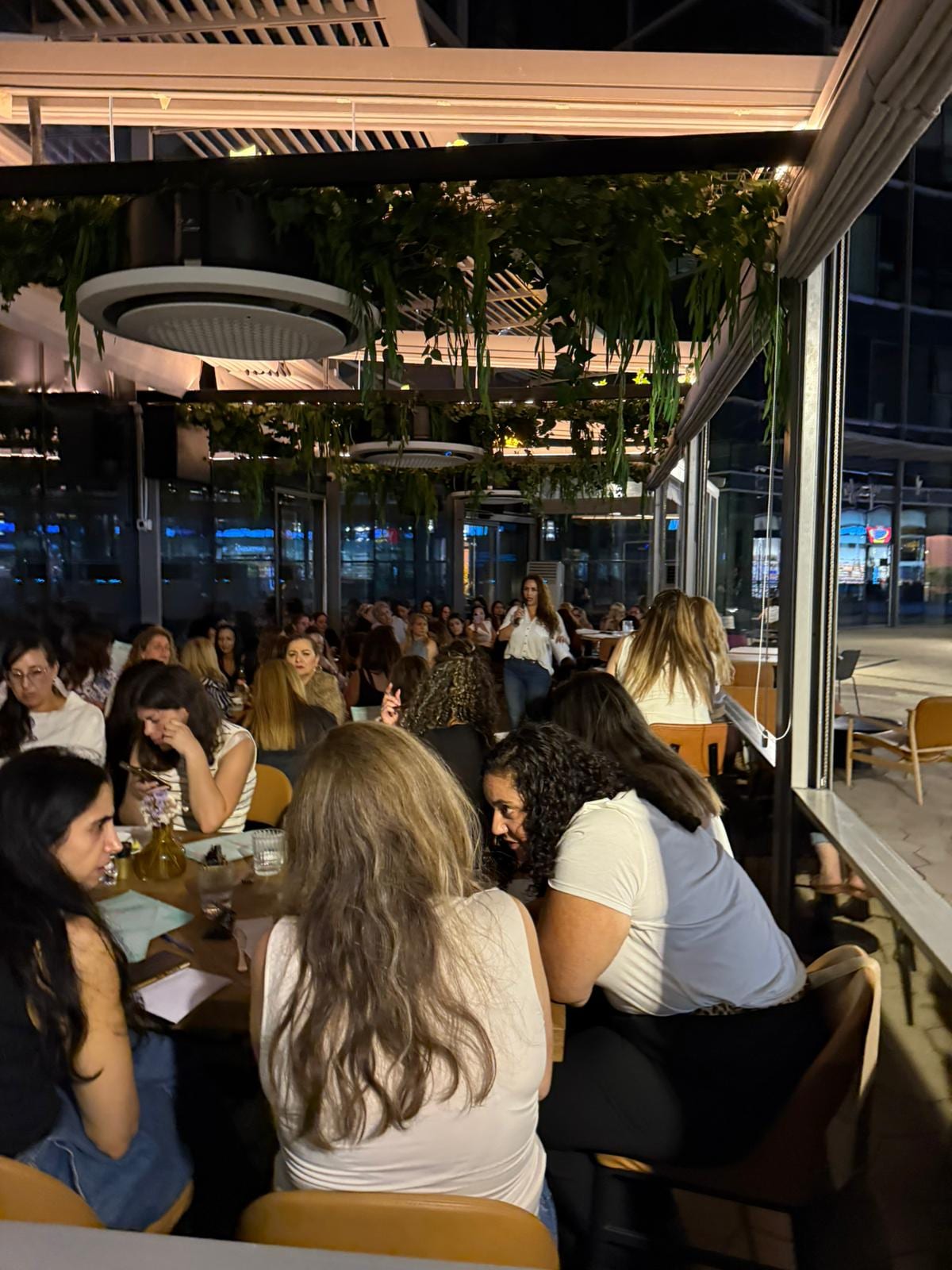 נשים יושבות סביב שולחנות ומדברות, המקום מלא